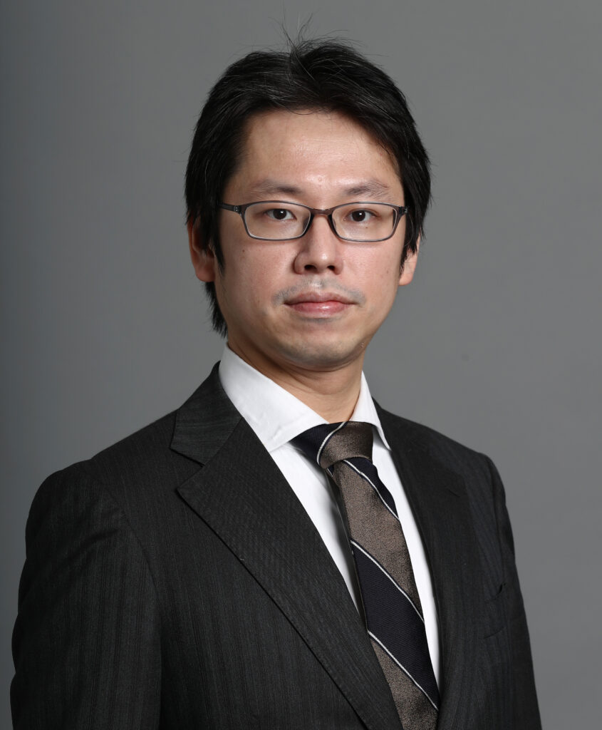 Portrait of a man wearing glasses and a dark pinstripe suit with a striped tie, facing the camera.