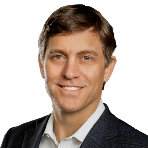 Smiling man in a dark blazer and white shirt, neutral black background (professional headshot).