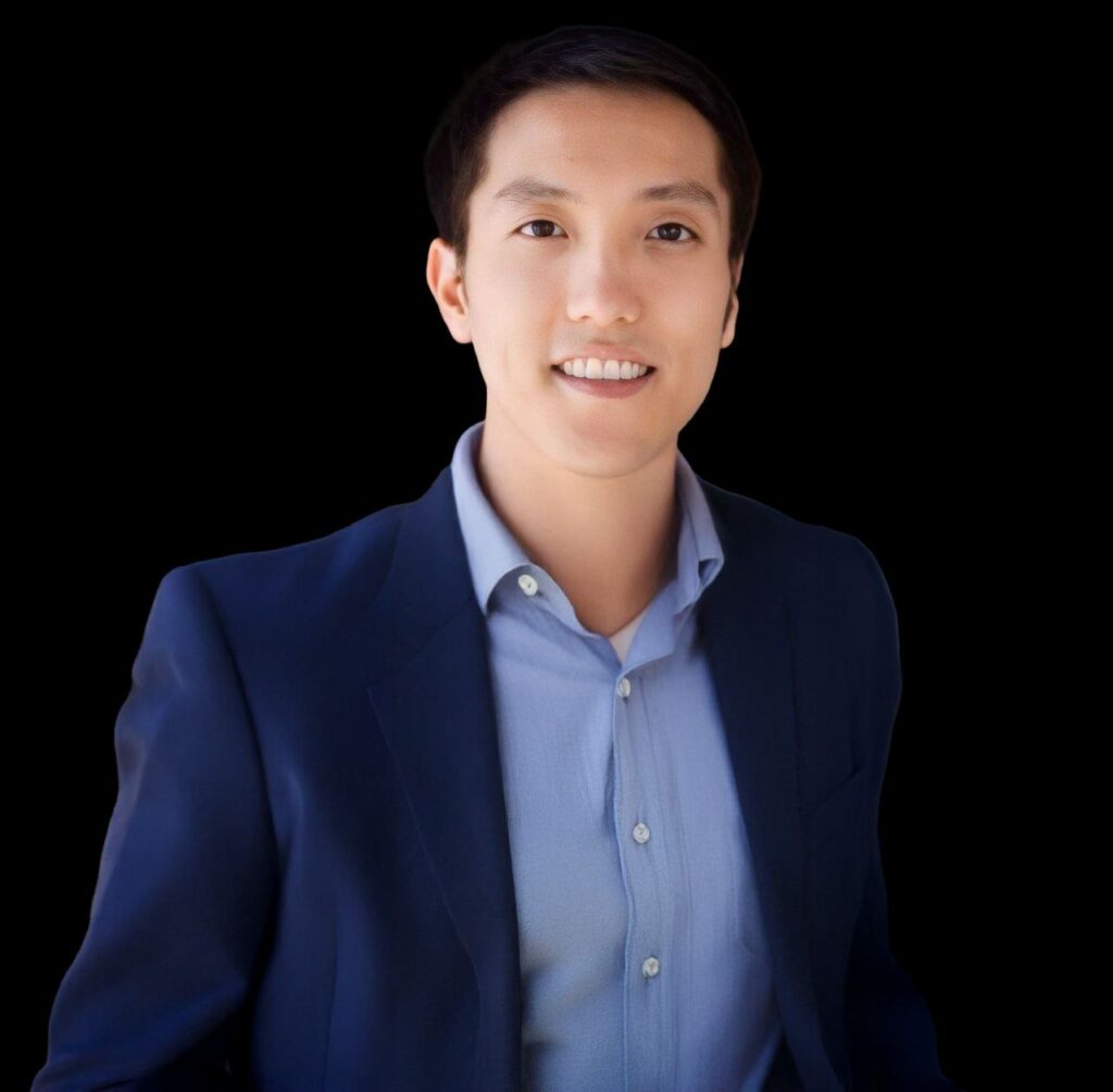 Professional portrait of a person in a navy blazer and light blue shirt, smiling against a black background.