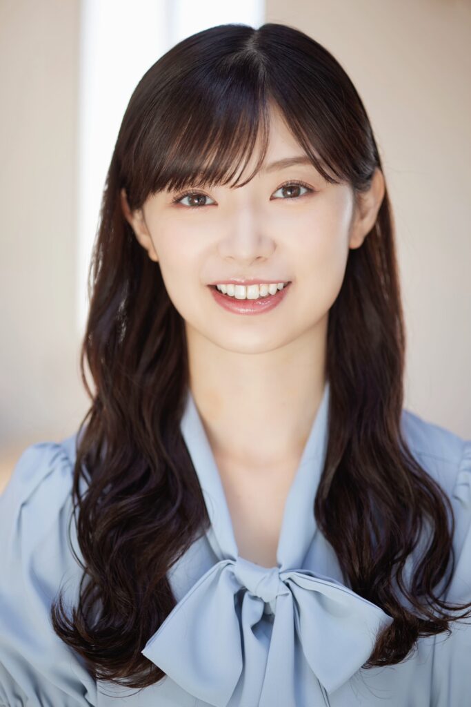 Smiling young woman with long dark hair wearing a light blue blouse with a bow, close-up portrait