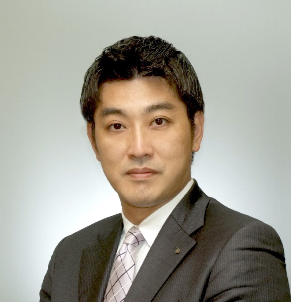 Professional headshot of a man in a dark suit and light pink tie, facing the camera against a plain light background.