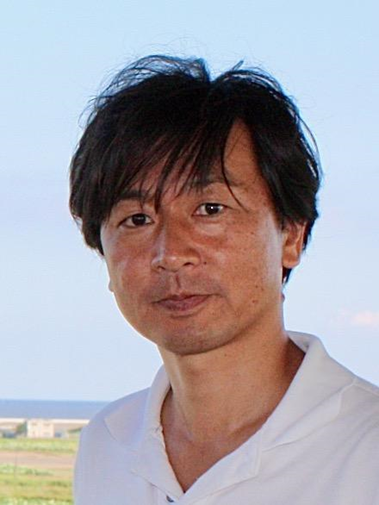 Portrait of an Asian man with dark hair wearing a white shirt, standing outdoors with the sea and sky in the background.